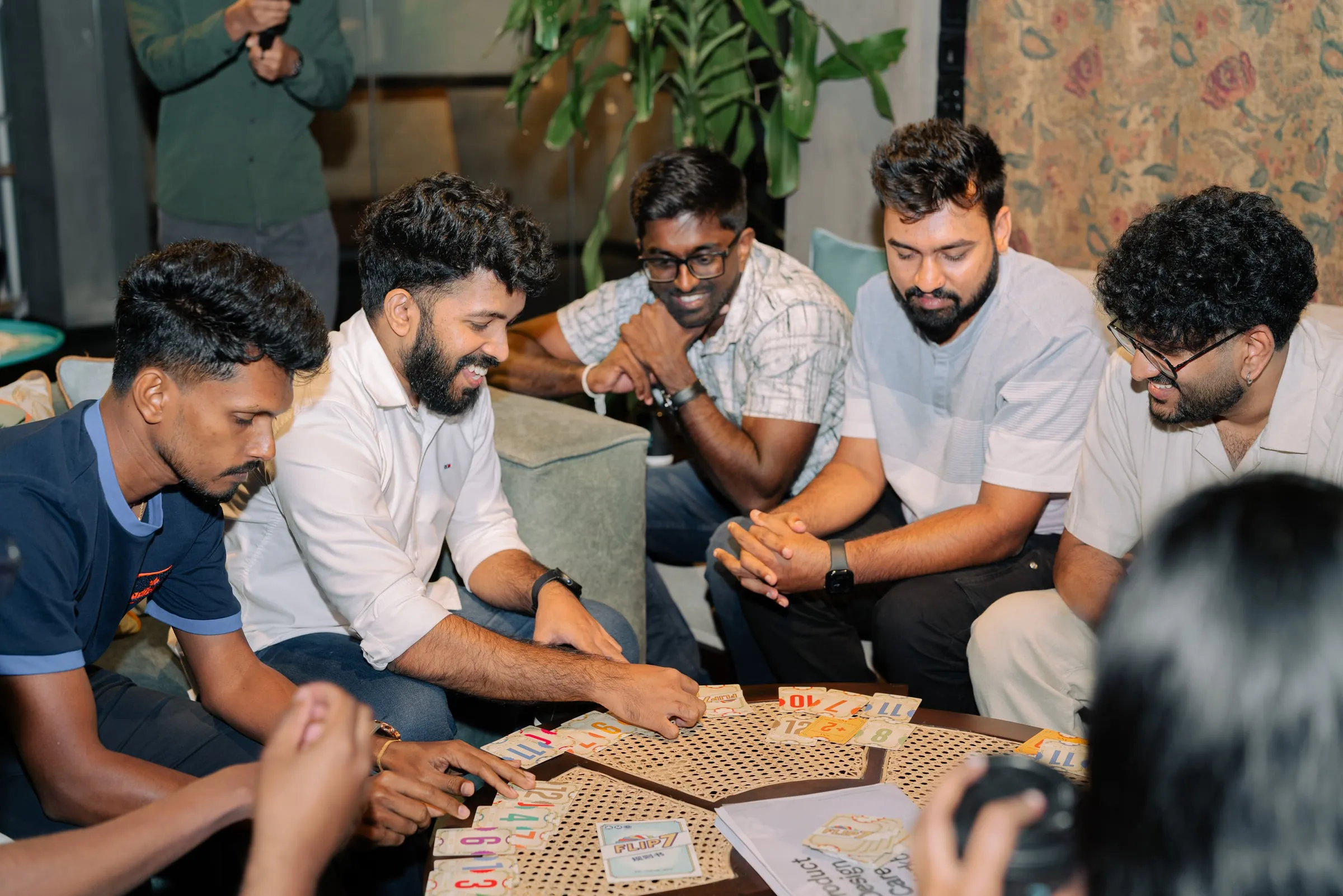 Six members around a low table, laughing over a card game.