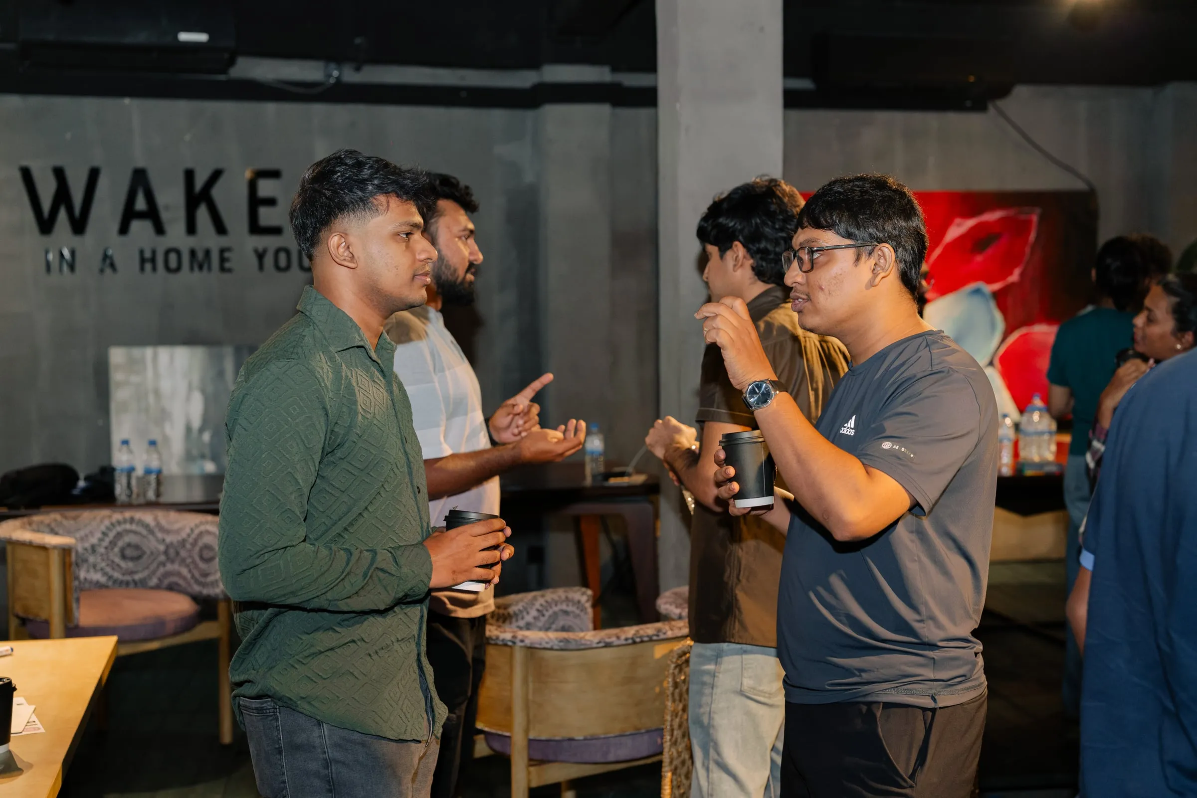Four members holding coffee cups in conversation, one of them gesturing as he makes a point.