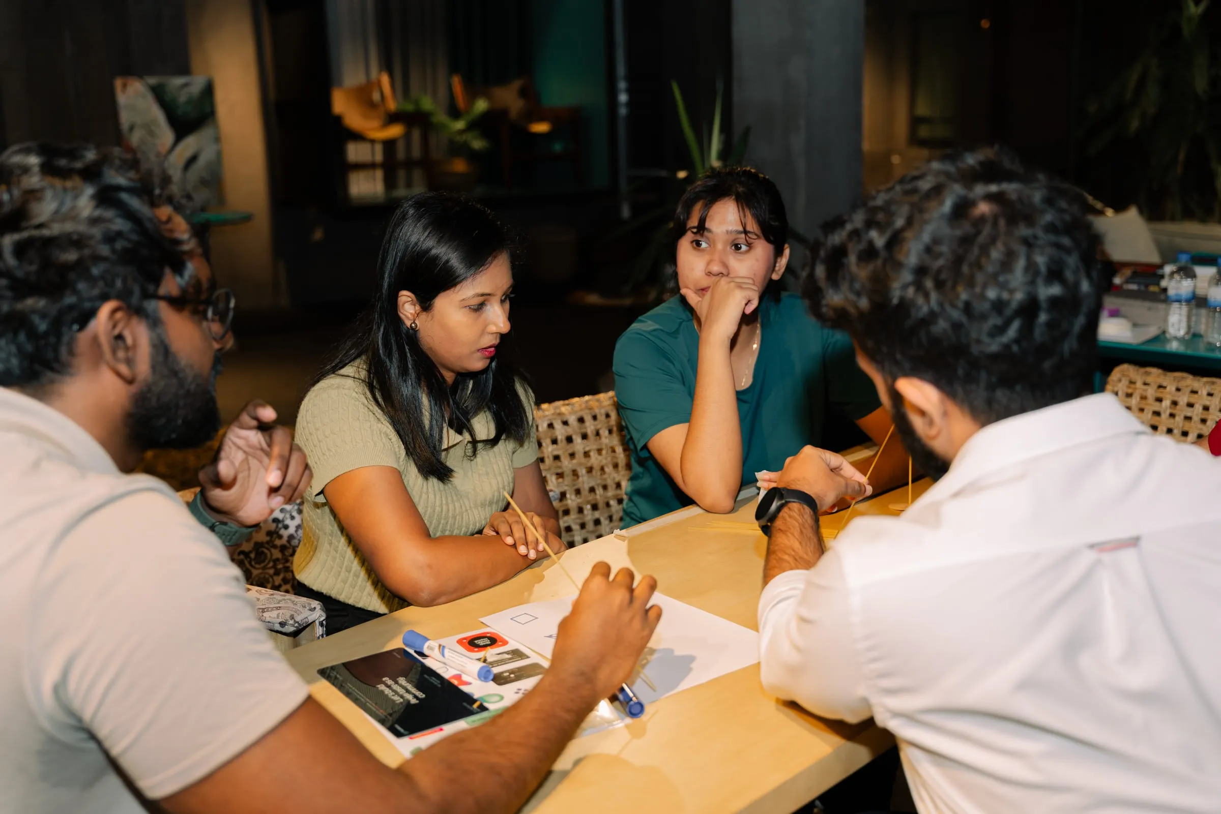 Four members around a café table working through a design exercise with paper and pens.